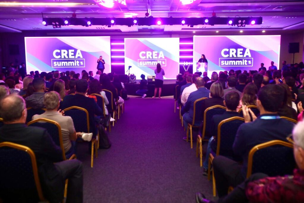 Auditório lotado no CREA Summit 2024, com um painel iluminado mostrando o nome do evento em destaque, realizado em Balneário Camboriú.